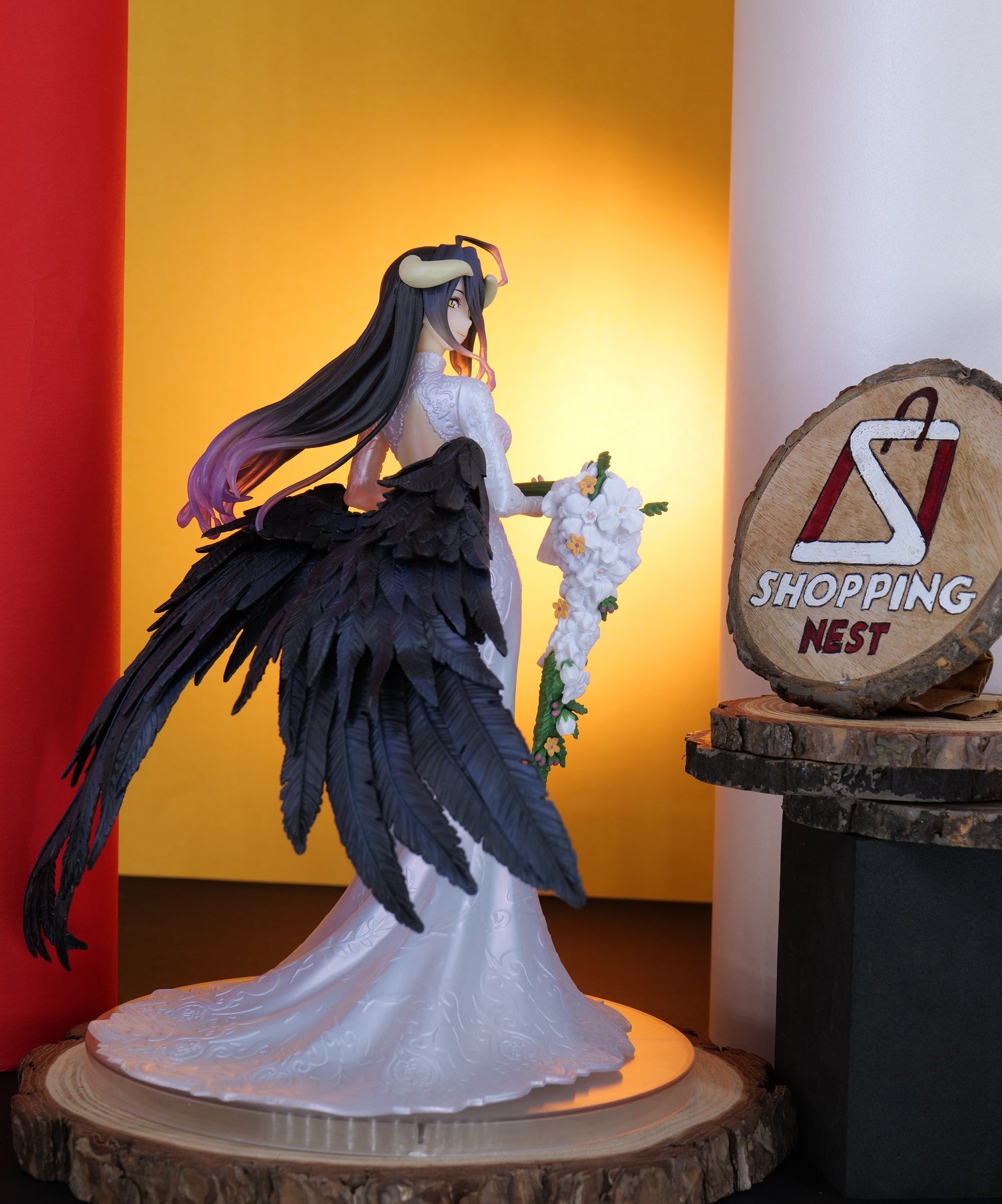 Statue of a character with black wings and white dress on a wooden base, with 'Shopping Nest' sign in the background.