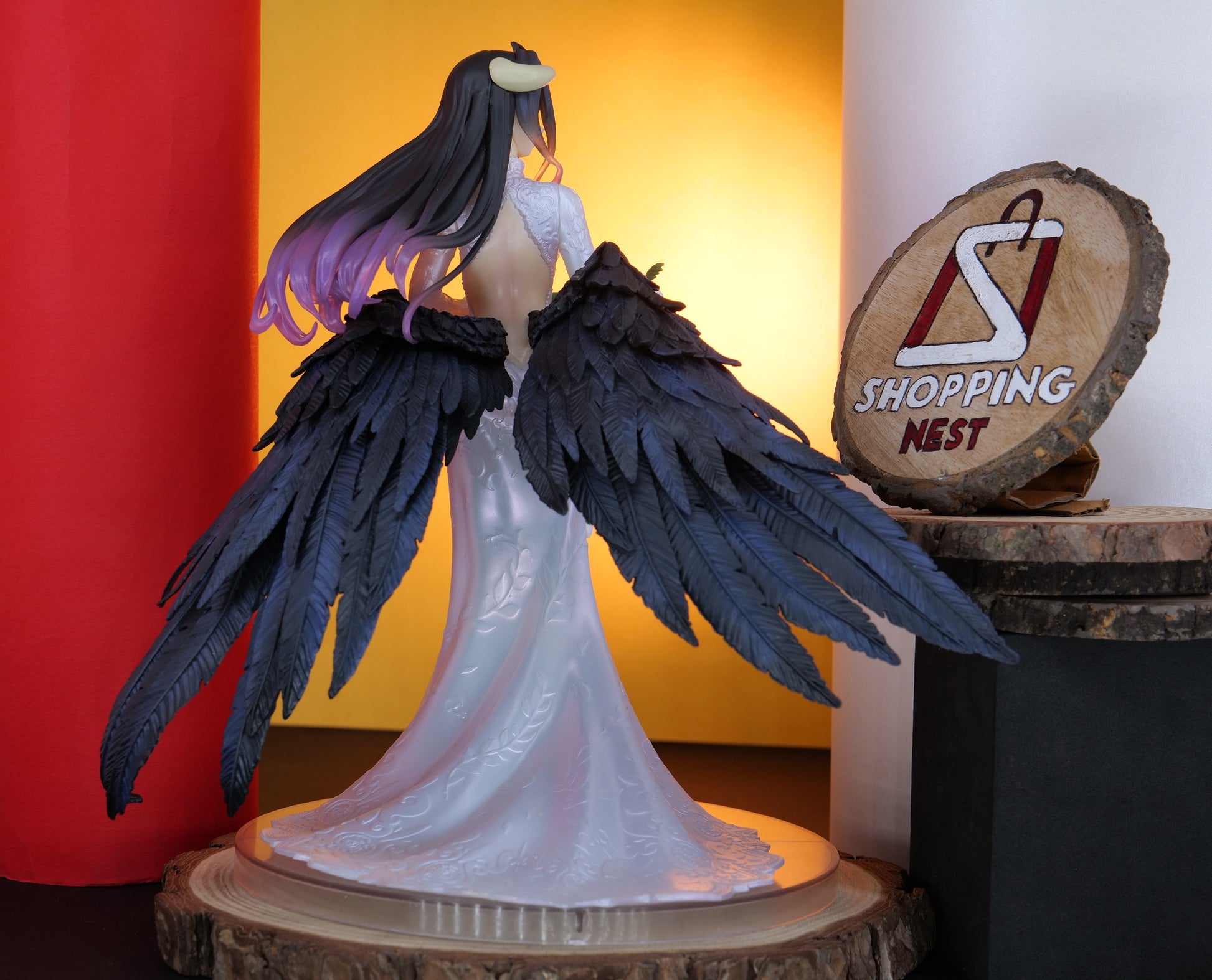 Figurine with large black wings on a wooden base, with 'Shopping Nest' logo in the background.