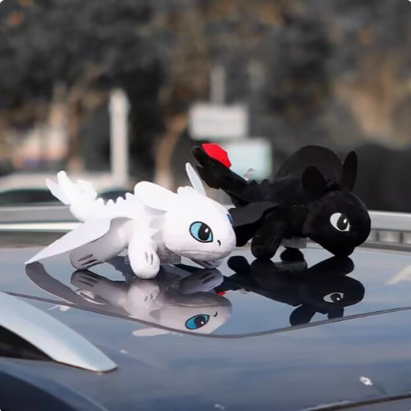 light furry, toothless ,Two dragon-shaped car dashboard toys, one white and one black, on a car's dashboard with a blurred outdoor background.